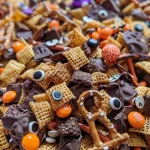 ['Close-up shot of colorful Halloween snack mix featuring cereals, pretzels, and candy.', 'Side view of a spooky snack mix with chocolate-coated treats and festive sprinkles.', 'Detailed image of Halloween-themed snack mix, including candy eyeballs and colorful candies.', 'Vibrant Halloween snack mix captured in a close-up photo, showcasing various sweet treats.']