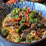 ['Close-up of Sticky Beef Noodles with vibrant bell pepper and greens.', 'Juicy sirloin steak slices over fresh egg noodles with broccoli and chilies.', 'A plate of Sticky Beef Noodles showcasing beef, colorful vegetables, and herbs.', 'Side view of a bowl filled with Sticky Beef Noodles garnished with spring onions.']