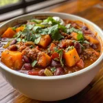 ['Close-up view of a bowl filled with vibrant sweet potato chili, featuring colorful ingredients.', 'A side view of a hearty sweet potato chili, showcasing diced sweet potatoes and various vegetables.', 'Delicious sweet potato chili in a rustic bowl, highlighting its texture and rich colors.', 'Close-up of a steaming bowl of sweet potato chili topped with fresh garnishes like lime and cilantro.']