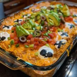['Close-up side view of Graveyard Taco Dip in a bowl, decorated with tombstone-shaped tortillas.', 'Juicy Graveyard Taco Dip layered with avocado, cheese, and salsa, featuring decorative toppings.', 'A vibrant, appetizing display of Graveyard Taco Dip with green onions and olives on top.', 'A tantalizing dish of Graveyard Taco Dip showing rich layers and unique tombstone tortilla shapes.']