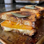 ['A side view of a juicy Butternut Squash Grilled Cheese sandwich with melted cheese oozing out.', 'Close-up of a Butternut Squash Grilled Cheese highlighting the golden-brown crust and vibrant filling.', 'Delicious Butternut Squash Grilled Cheese with layers of cheese and squash visible from the side.', 'A mouthwatering Butternut Squash Grilled Cheese sandwich showcasing its cheesy texture and crispy bread.']