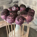 ['Side view of delicious Vampire Cake Pops decorated with dark chocolate and fruit roll-ups.', 'Close-up photo of Vampire Cake Pops featuring a mix of black and tan chocolate coatings.', 'Juicy Vampire Cake Pops displayed on a Styrofoam block, showcasing creative chocolate designs.', 'Intricate side view of cake pops resembling vampires, complete with chocolate and candy details.']