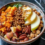 ['A colorful Vegan Fall Harvest Farro Bowl featuring roasted butternut squash, sliced apples, chickpeas, and topped with pumpkin seeds and cranberries.', 'Close-up view of a Vegan Fall Harvest Farro Bowl displaying layers of vibrant vegetables, fruits, nuts, and a drizzle of ranch dressing.', 'Side view of a beautifully arranged Vegan Fall Harvest Farro Bowl with butternut squash, apples, chickpeas, and garnishes.', 'A hearty Vegan Fall Harvest Farro Bowl filled with roasted vegetables, chickpeas, dried cranberries, and pumpkin seeds.']